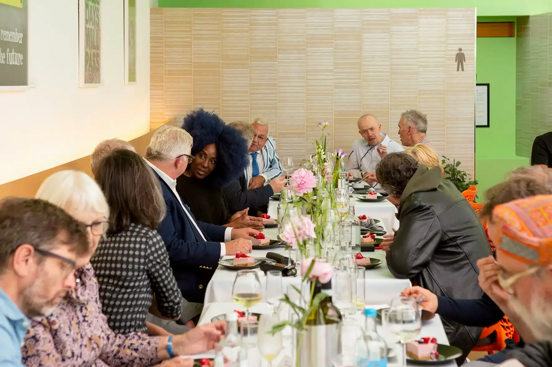 People sitting around a long rectangle table with a white cloth and flowers, food and drinks on top at the Berryfield Cafe.